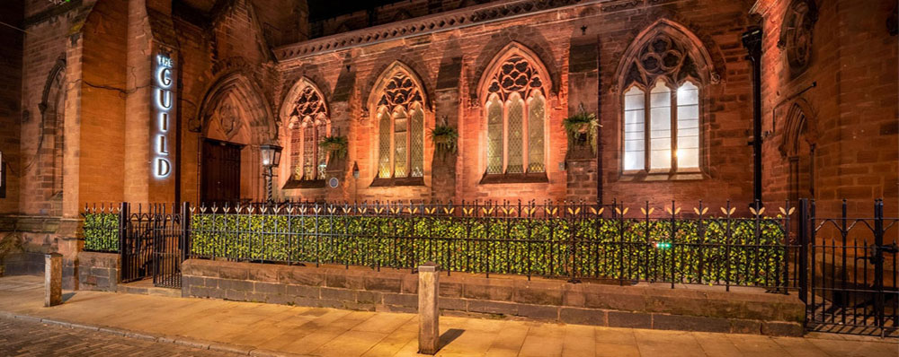 outside of the guild converted church at night with long faux hedge next to railings