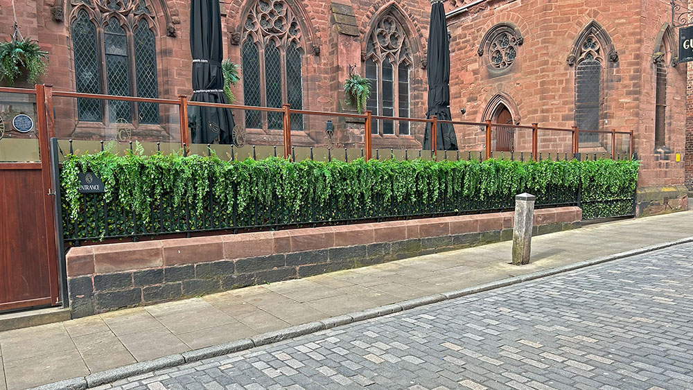 outside of the guild converted church daytime with long faux hedge next to railings