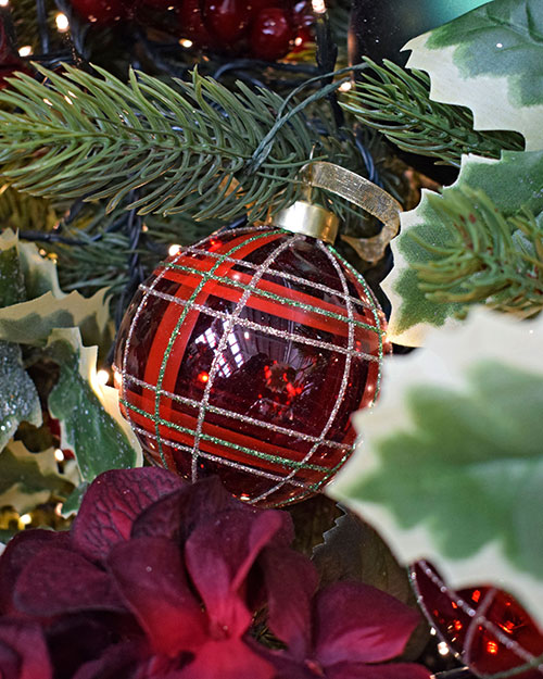 close up of red tartan bauble on tree with holly