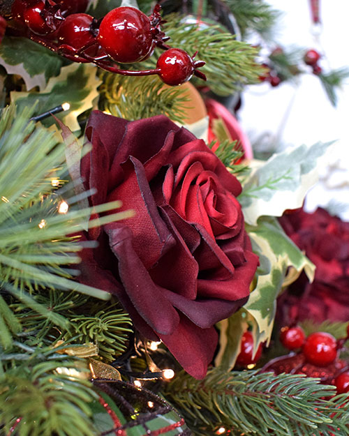 close up of artificial burgundy rose and red berries in traditional christmas tree