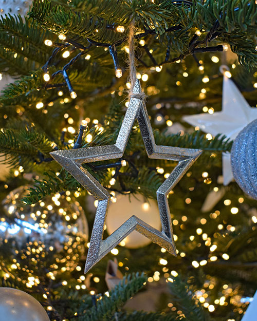close up of silver and white star decorations on christmas tree with lights