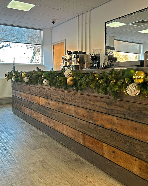 college wooden panel coffee bar with green garland, gold, green, and white baubles with foliage patterns