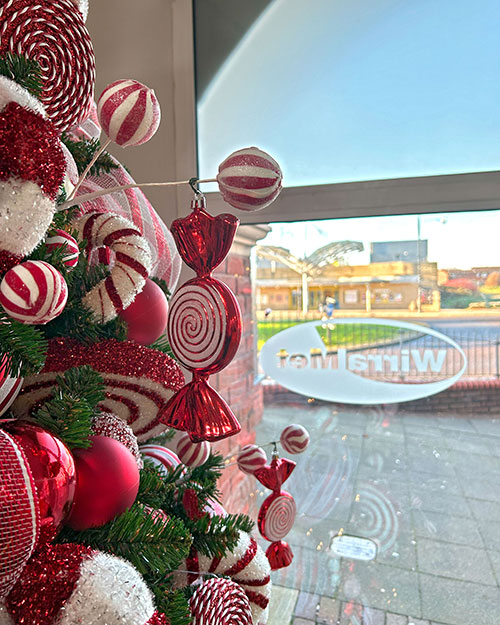 close up of candy cane themed christmas decorations on green tree near wirral met college window with logo