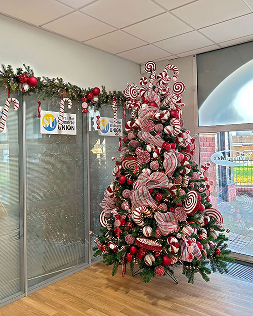 large green christmas tree and garland decorated with a candy cane theme next to wirral met college student union