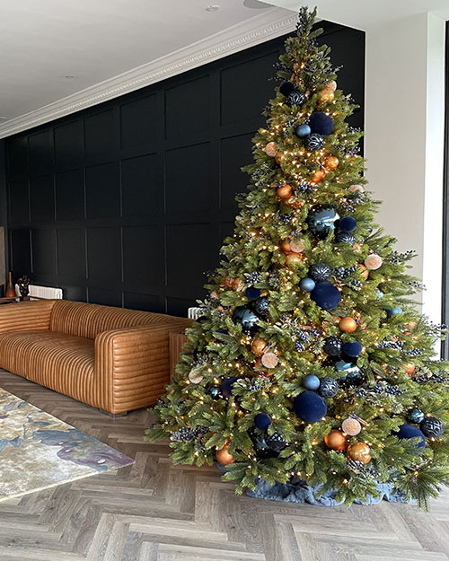 large oregon pine artificial christmas tree with blue and copper decorations next to tan sofa