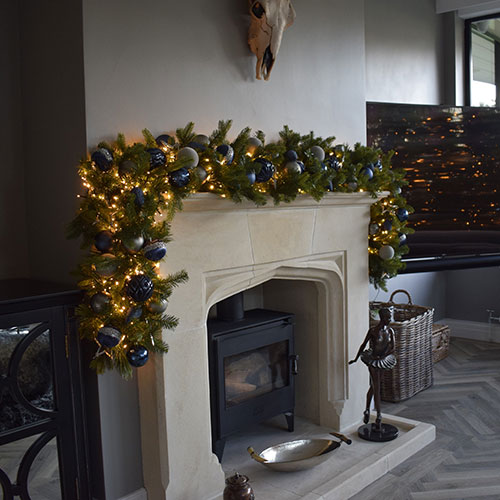 lounge with christmas garland over fireplace decorated with blue, grey and silver baubles