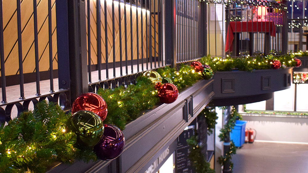 green artificial Christmas garland with fairy lights and giant baubles along commercial balcony
